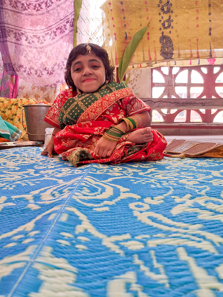 Young disabled woman in a colourful sari sitting on a blue and cream woven plastic mat