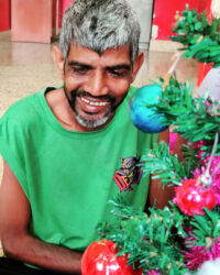 shuktara - man in bright green shirt next to an artificial Christmas tree
