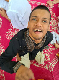young man in black kurta sitting with red and gold fabric behind him