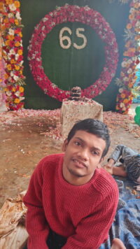 young man in red jumper with a flower board behind him