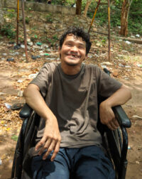 Young man in wheelchair smiling; with trees behind him