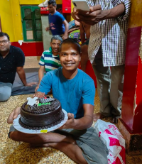 young man in blue shirt holding birthday cake with chocolate icing
