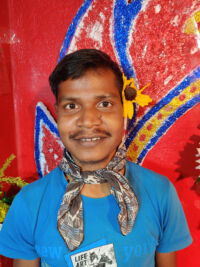 shuktara - young man in blue shirt standing in front of a bright painting smiling